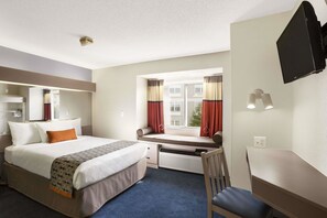 Une chambre d’hôtel équipée d’un lit, d’un bureau, d’une chaise, d’un téléviseur fixé au mur et d’une fenêtre avec des rideaux.