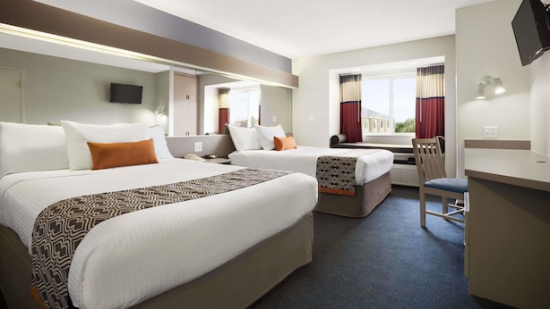 Ein Hotelzimmer mit zwei Betten, einem Schreibtisch, einem Stuhl, einem Fernseher und einem großen Fenster mit Vorhängen.