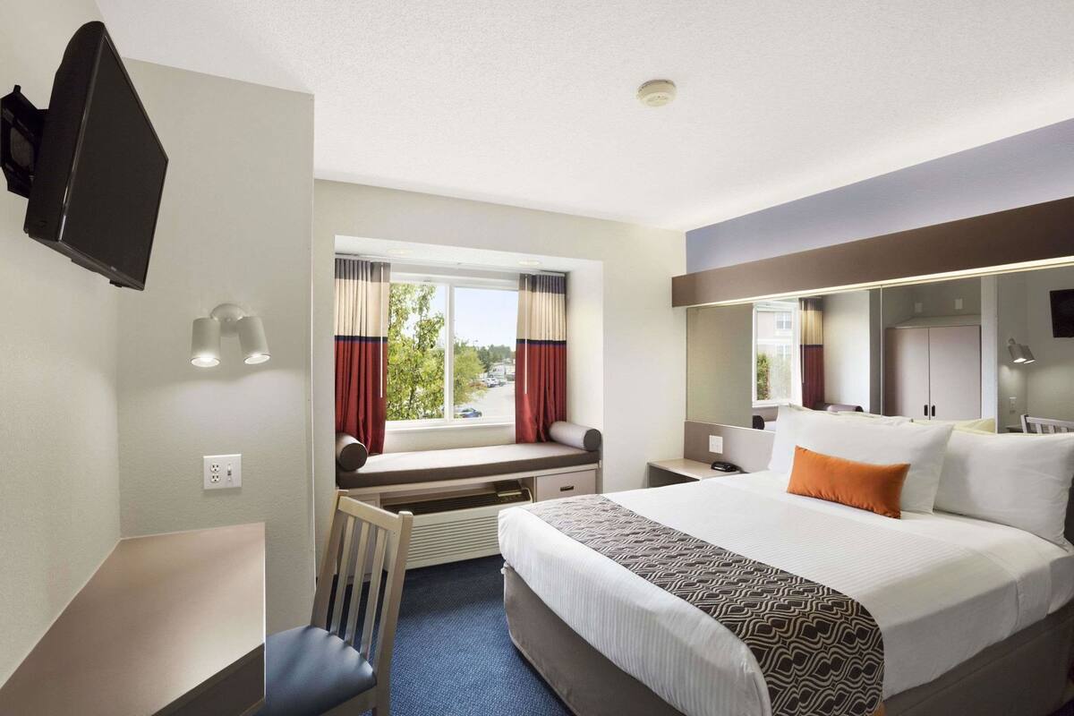 Une chambre d’hôtel comprenant un lit, un bureau, une chaise, une télévision, une fenêtre avec des rideaux et un miroir.