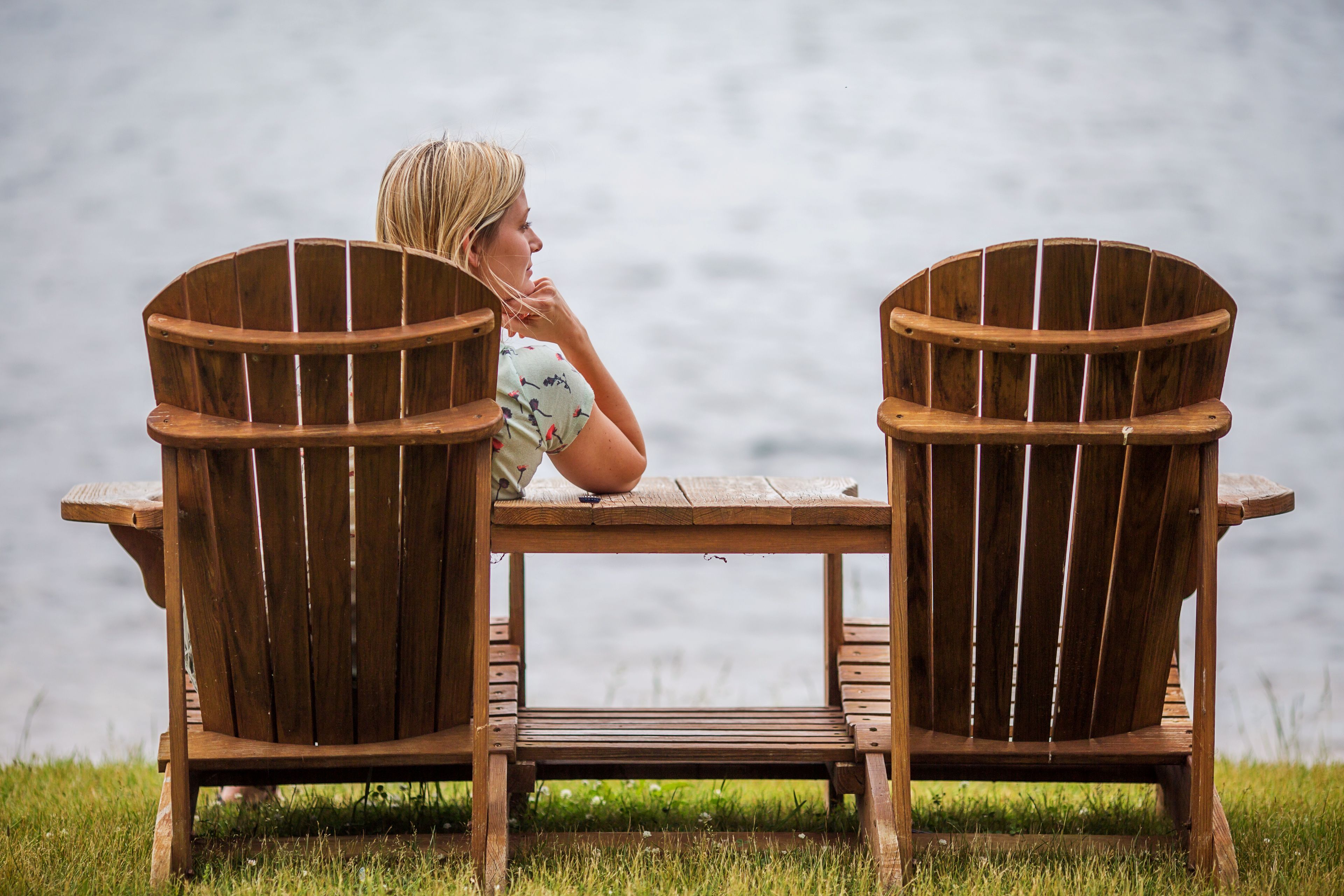 Two wooden Adirondack chairs facing a body of water.