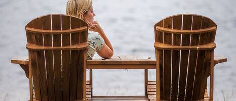 Two wooden Adirondack chairs facing a body of water.