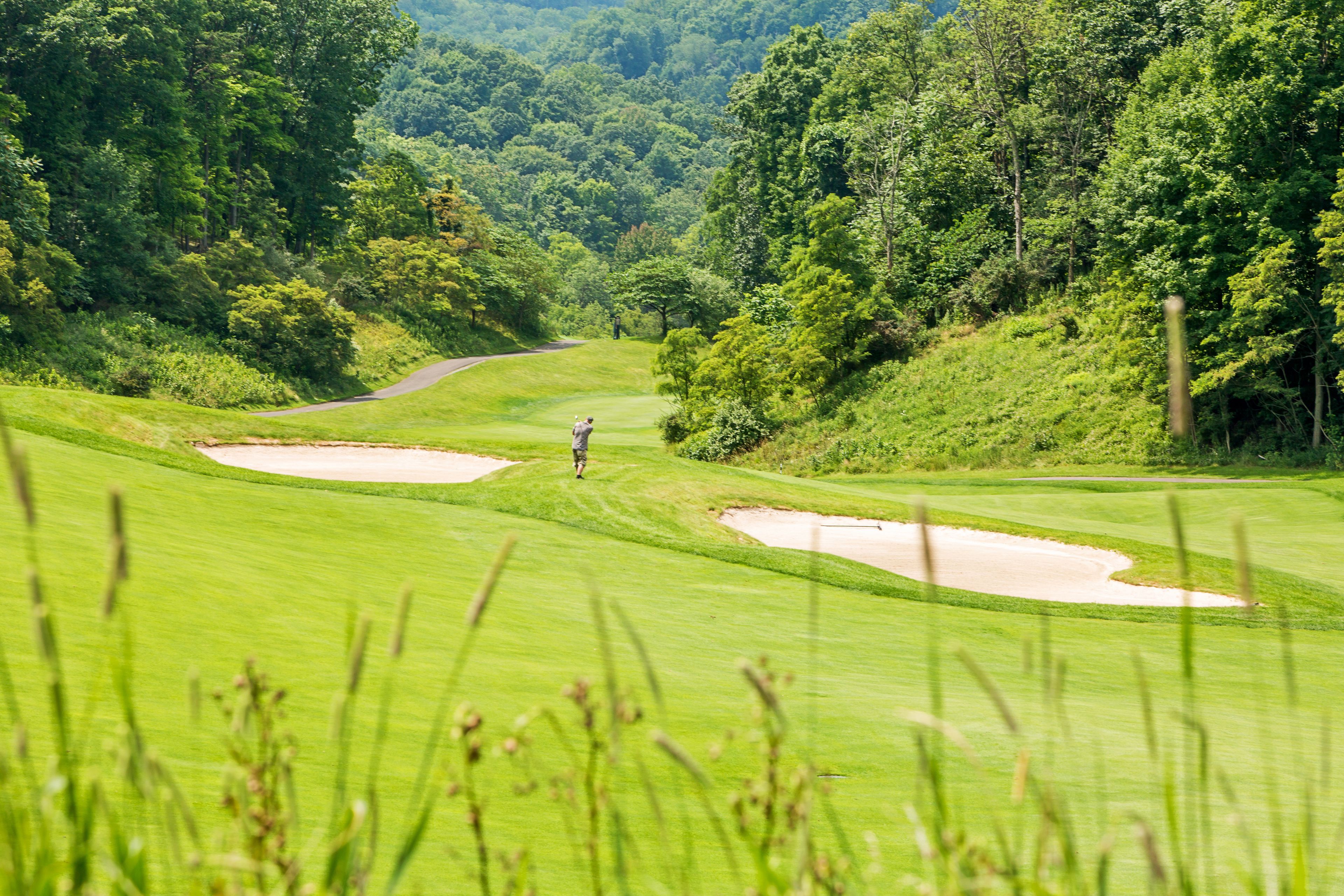 A golf course with a well-maintained fairway, sand bunkers, and dense forested areas.