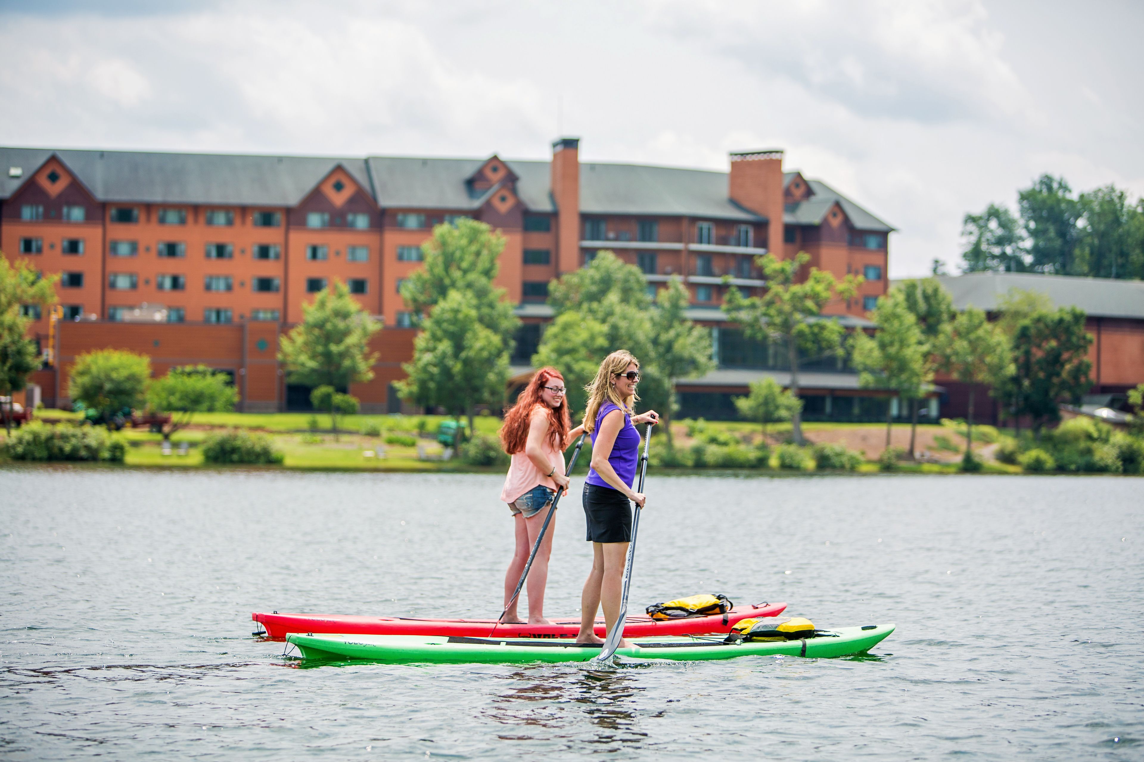Two people standing on a paddleboard in a body of water with a large building in the background.