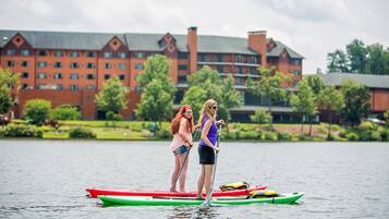 Two people standing on a paddleboard in a body of water with a large building in the background.