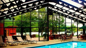 An indoor swimming pool with a glass enclosure, lounge chairs, and tables. - Rocky Gap Casino & Resort (Cumberland)