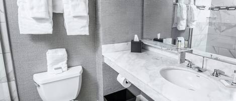 A modern bathroom with a toilet, sink, and mirror. There are towels hanging on a rack and a black trash bin under the sink.
