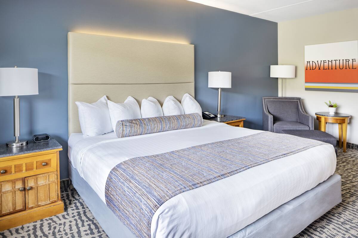 A hotel room with a large bed, two bedside tables with lamps, a chair, and a wall art piece.