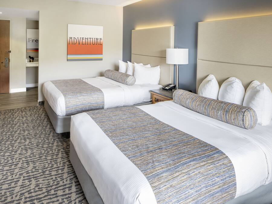 A hotel room with two beds, a nightstand, a lamp, and a wall-mounted artwork.