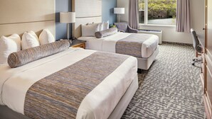 A hotel room with two beds, a large window with a view of greenery, a desk with a lamp, and a chair. - Rocky Gap Casino & Resort (Cumberland)
