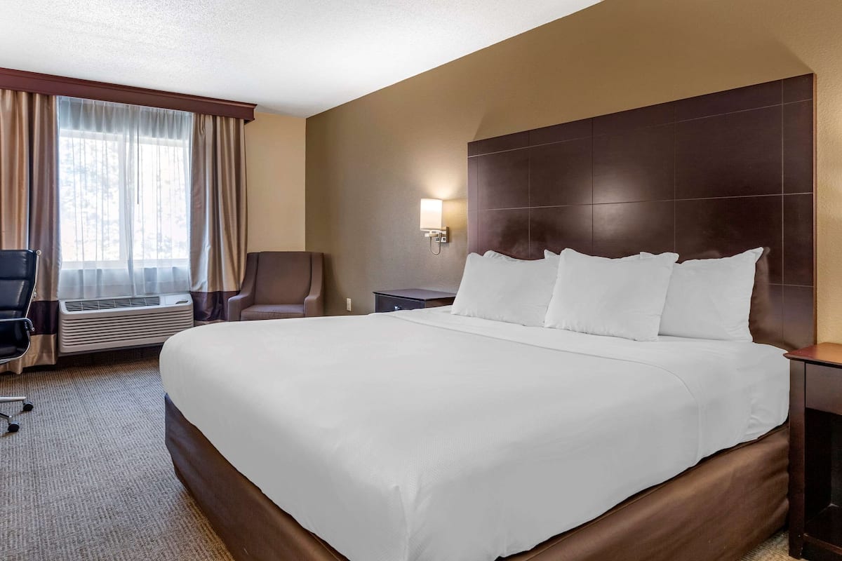 Ein Hotelzimmer mit einem großen Bett, einem Schreibtisch, einem Stuhl und einem Fenster mit Vorhängen.