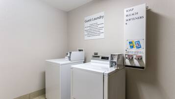 A guest laundry area with two washing machines and a coin-operated soap, bleach, and softener dispenser.