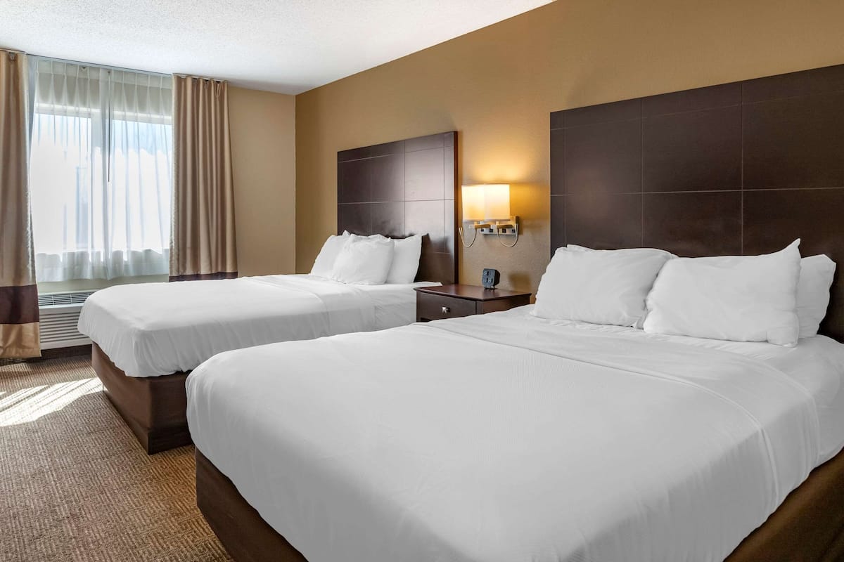 Ein Hotelzimmer mit zwei Betten, einem Nachttisch, einer Lampe und einem Fenster mit Vorhängen.