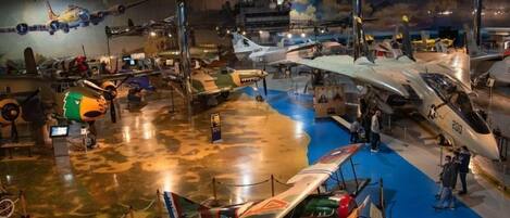Un musée où sont exposés divers types d’aéronefs, notamment des avions de chasse et un avion de combat à la livrée rouge et bleue distinctive.