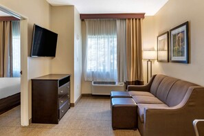 A hotel room with a flat-screen TV mounted on the wall, a sofa, a small table, a dresser, and a window with curtains. - Comfort Inn & Suites Paw Paw (Paw Paw)