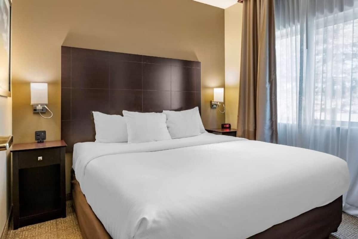 Ein Hotelzimmer mit einem großen Bett, zwei Nachttischen, einer Kopfteil und einem fenster mit Vorhängen.