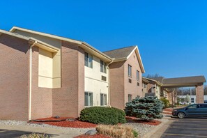 A multi-story hotel with brick exterior, a covered parking area, and a small evergreen tree in the foreground. - Comfort Inn & Suites Paw Paw (Paw Paw)