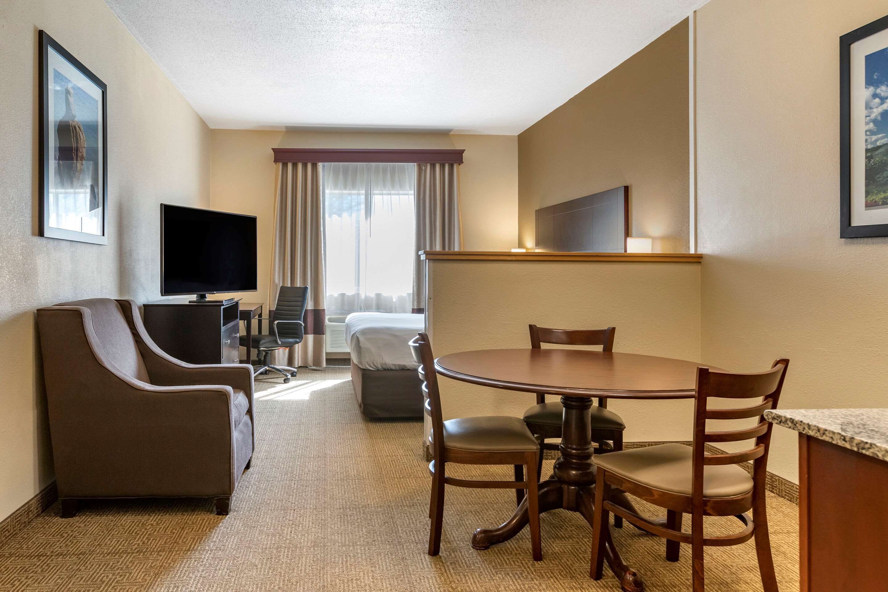 A hotel room with a large bed, a desk, a TV, a sofa, and a dining table with chairs.