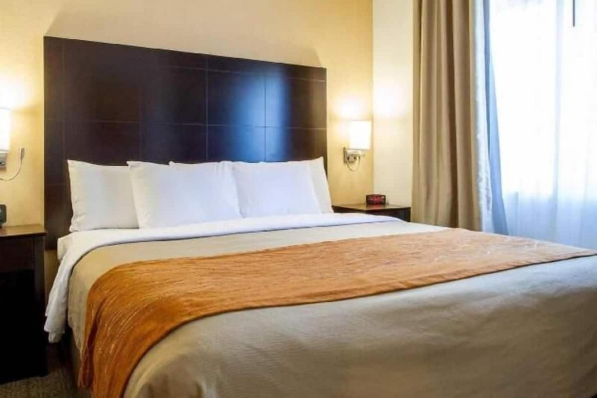Ein Hotelzimmer mit einem großen Bett, einem dunklen Kopfteil, zwei Nachttischen mit Lampen und einem Fenster mit Vorhängen.