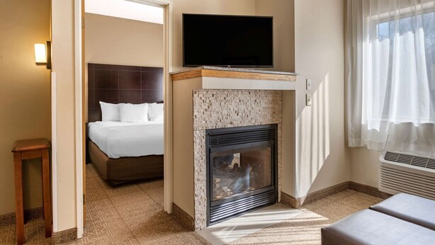 Une chambre d’hôtel avec un lit, un téléviseur fixé au-dessus d’une cheminée et une fenêtre avec des rideaux.
