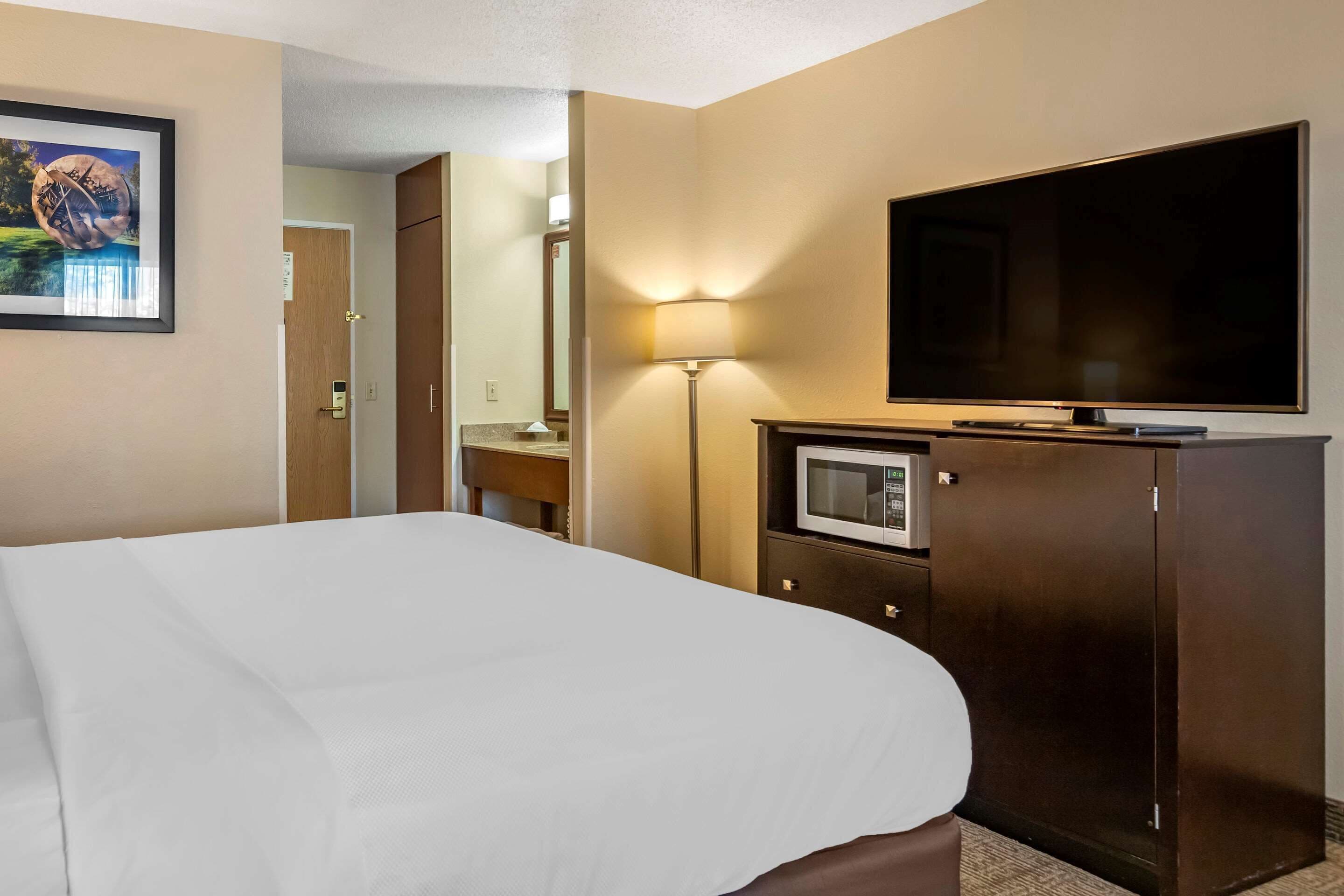 Una camera d'albergo con un letto, una TV, un forno a microonde e una porta che dà su un'altra stanza.