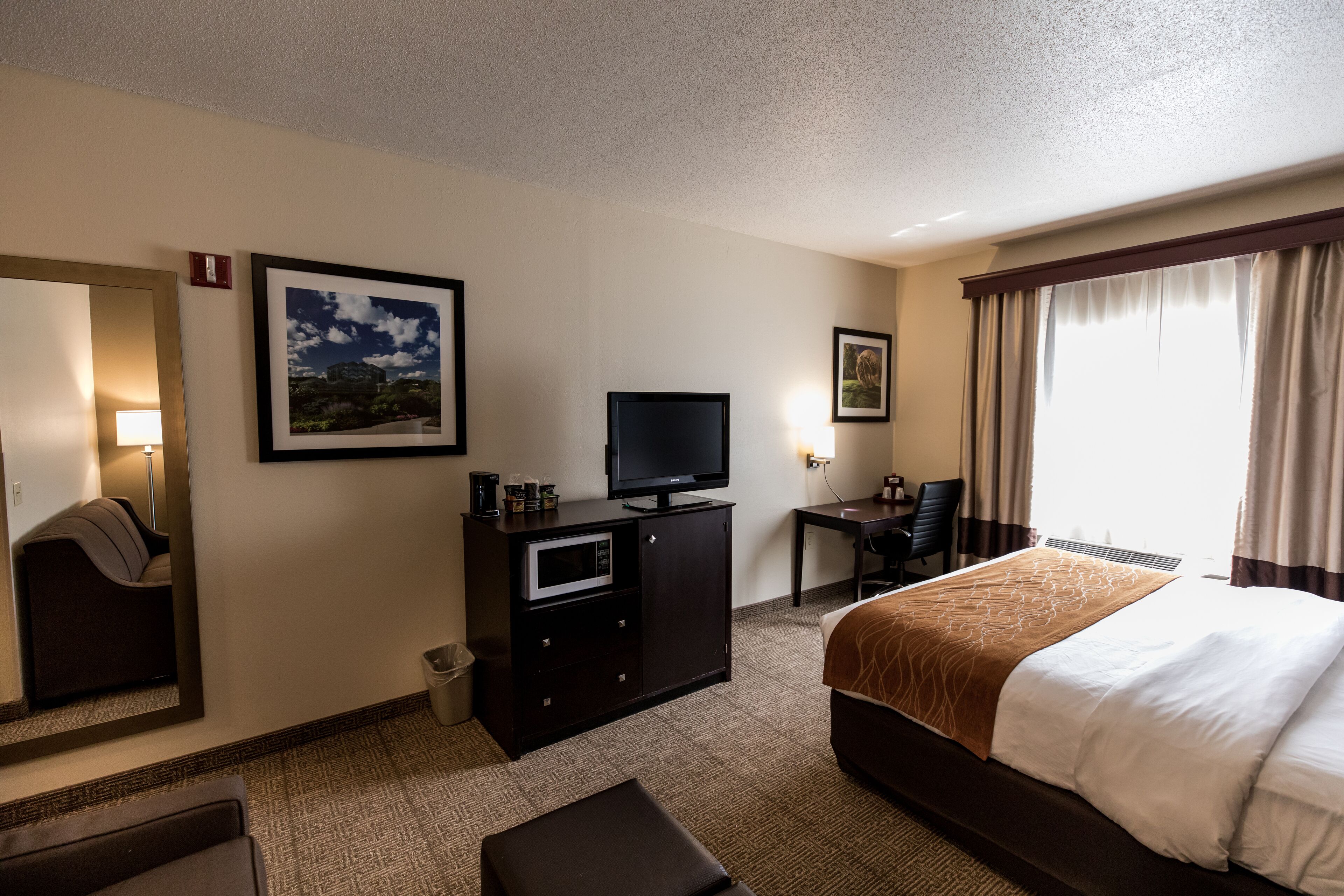 A hotel room with a bed, a desk, a television, a chair, and a mirror.
