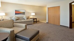 A hotel room with a sofa, a chair, a small table, a lamp, a painting on the wall, and a closet. - Holiday Inn Express St Paul S - Inver Grove Hgts by IHG (Inver Grove Heights)