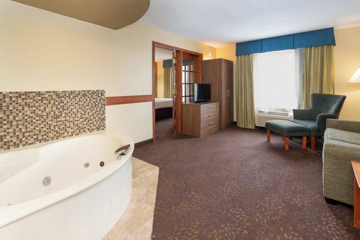 A hotel room with a bathtub, a television, a sofa, a chair, and a wardrobe.