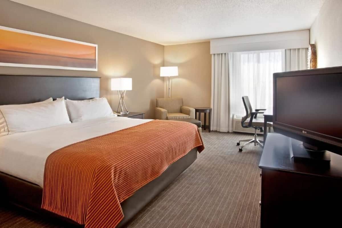 A hotel room with a large bed, two bedside lamps, a television, a desk, and a chair.
