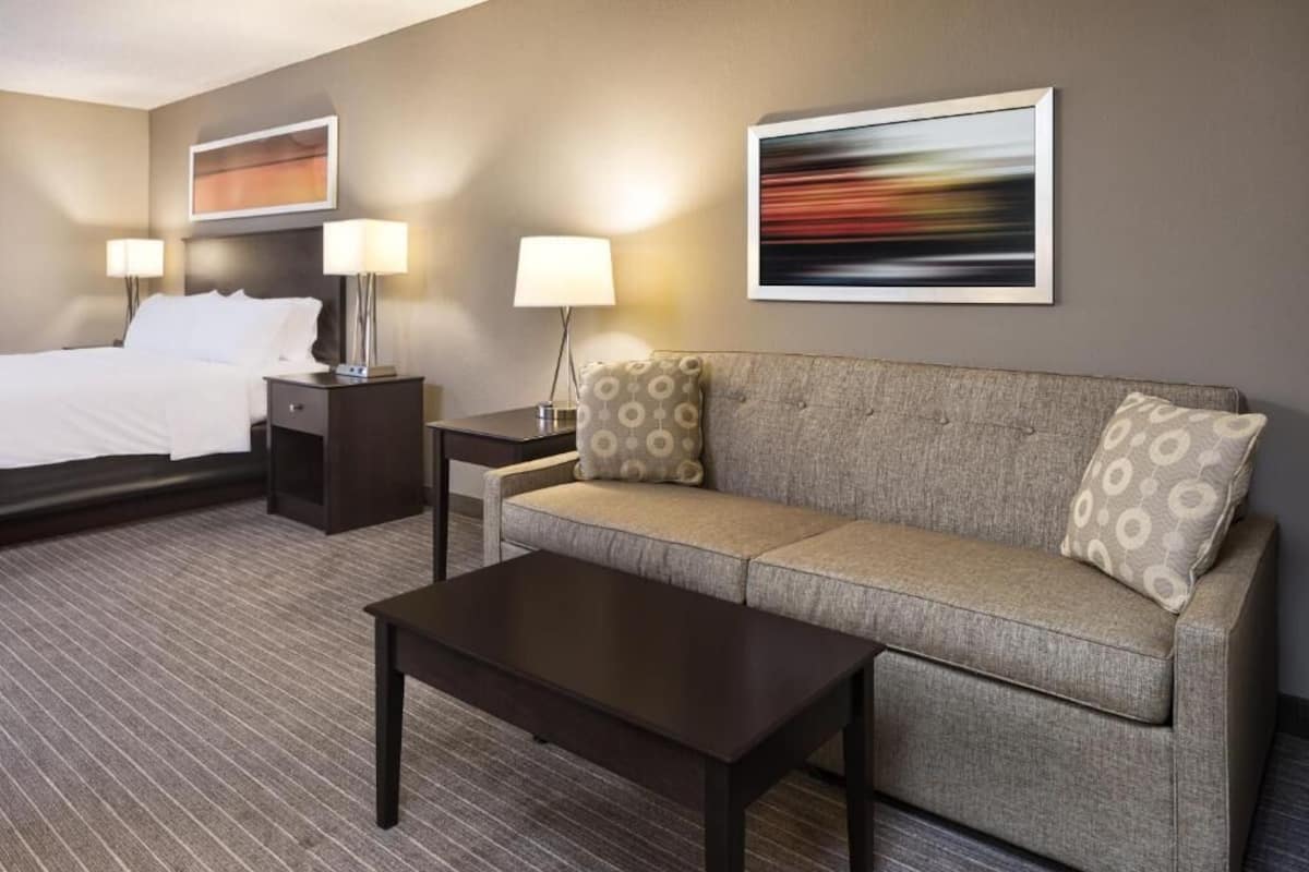 A hotel room with a bed, a sofa, a coffee table, a nightstand, and two lamps.