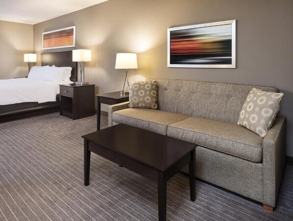 A hotel room with a bed, a sofa, a coffee table, a nightstand, and two lamps. - Holiday Inn Express St Paul S - Inver Grove Hgts by IHG (Inver Grove Heights)
