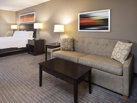 Una habitación de hotel con cama, sofá, mesa de centro, mesita de noche y dos lámparas.