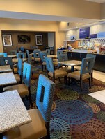 Un comedor de hotel con mesas y sillas, una barra de buffet y una alfombra estampada.