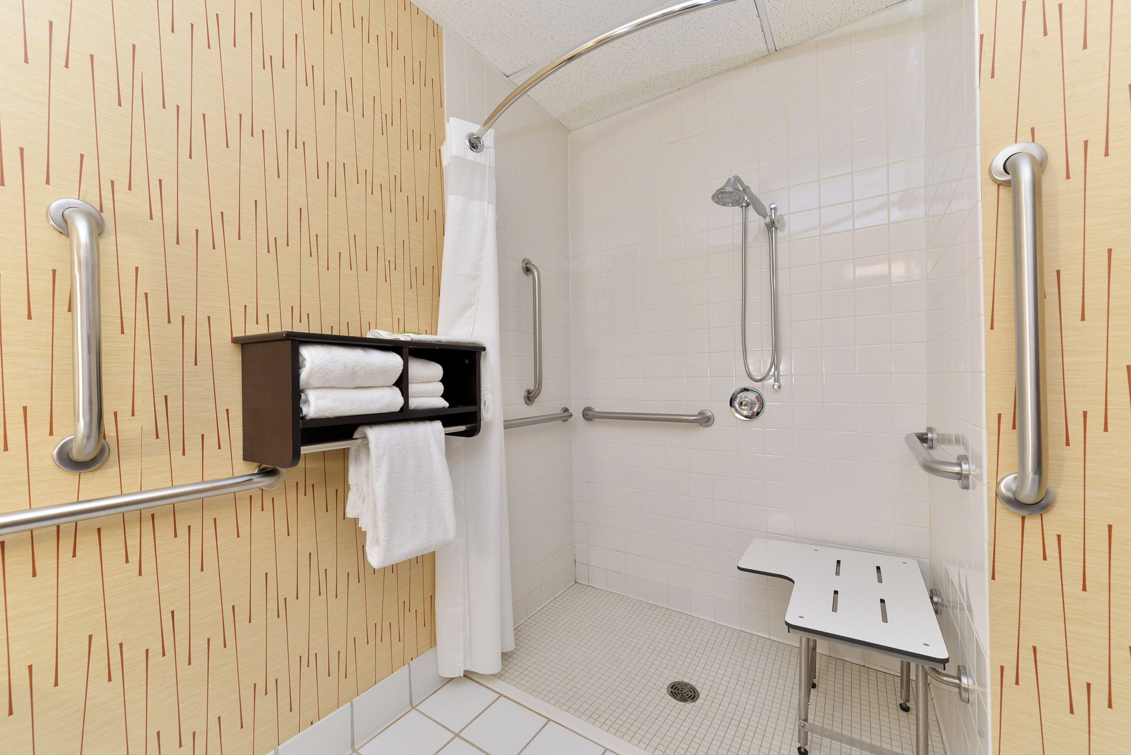 Un espace douche équipé d’une barre d’appui, d’un lavabo blanc et d’un porte-serviettes.