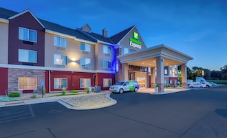 Un hotel Holiday Inn Express con diseño moderno, que cuenta con un acceso cubierto y varios espacios de estacionamiento.