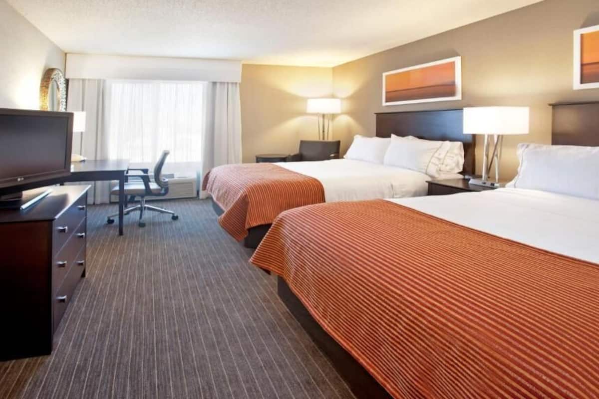 A hotel room with two beds, a desk, a television, and a chair.