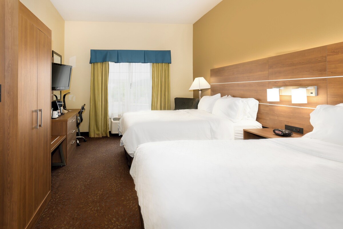 A hotel room with two beds, a desk with a computer, a TV, and a window with curtains.