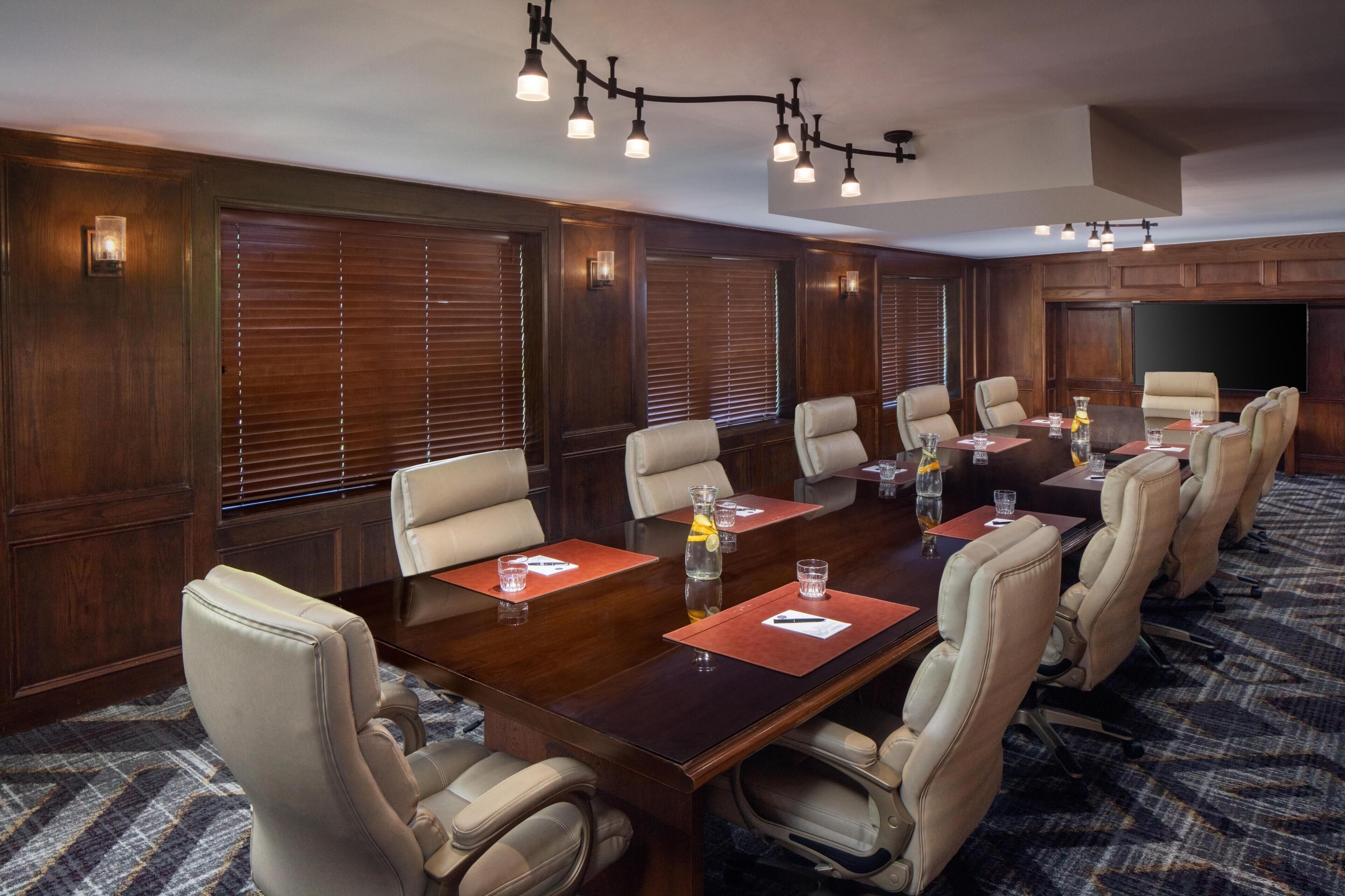 A conference room with a long table, multiple chairs, and a large screen.
