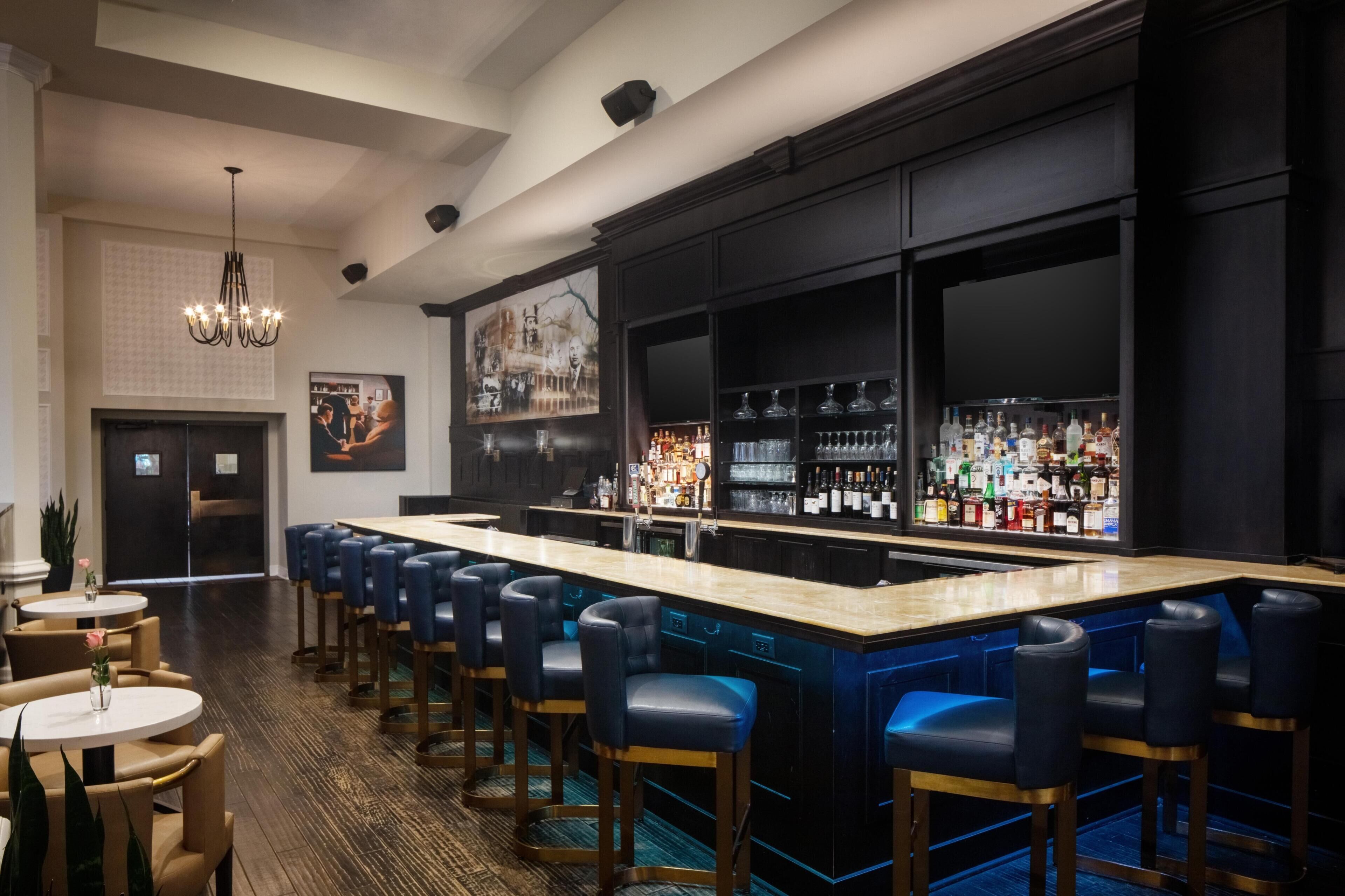 A bar area with a long counter, multiple bar stools, and a variety of bottles.