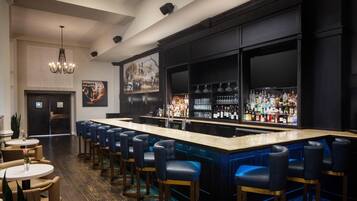 A bar area with a long counter, multiple bar stools, and a variety of bottles.