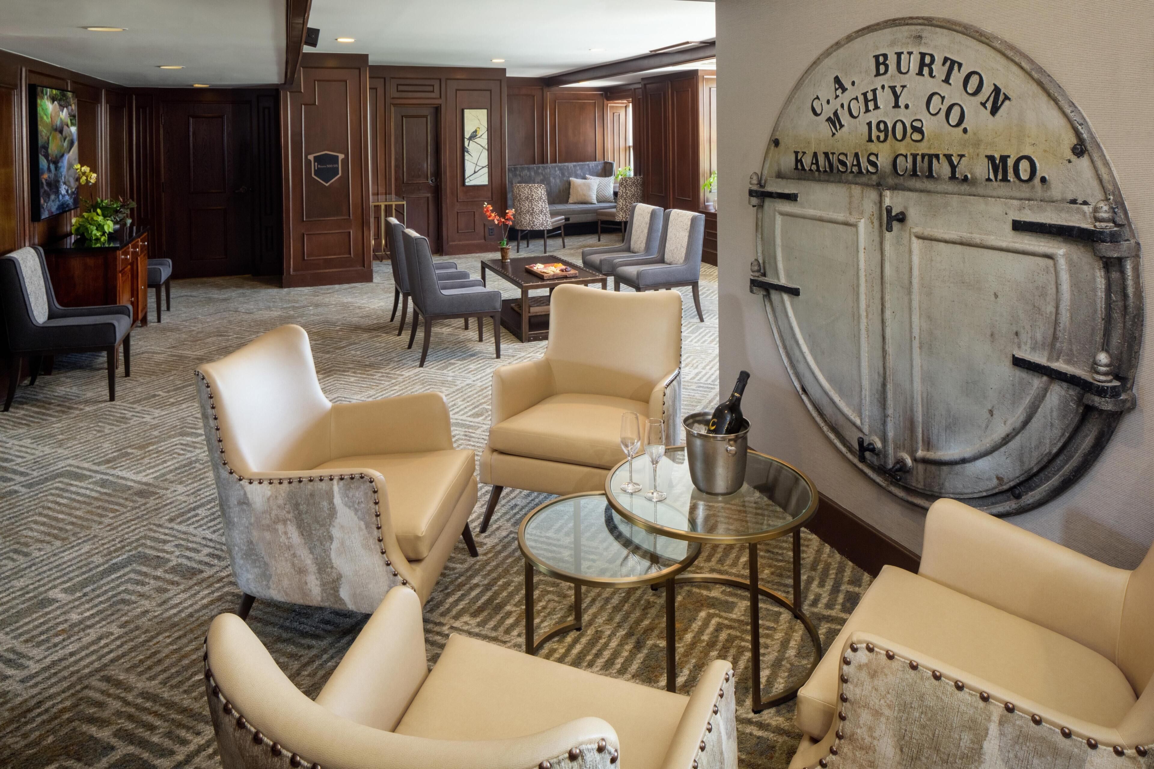 A hotel lobby with leather armchairs, a sofa, a coffee table, and a wall-mounted sign.