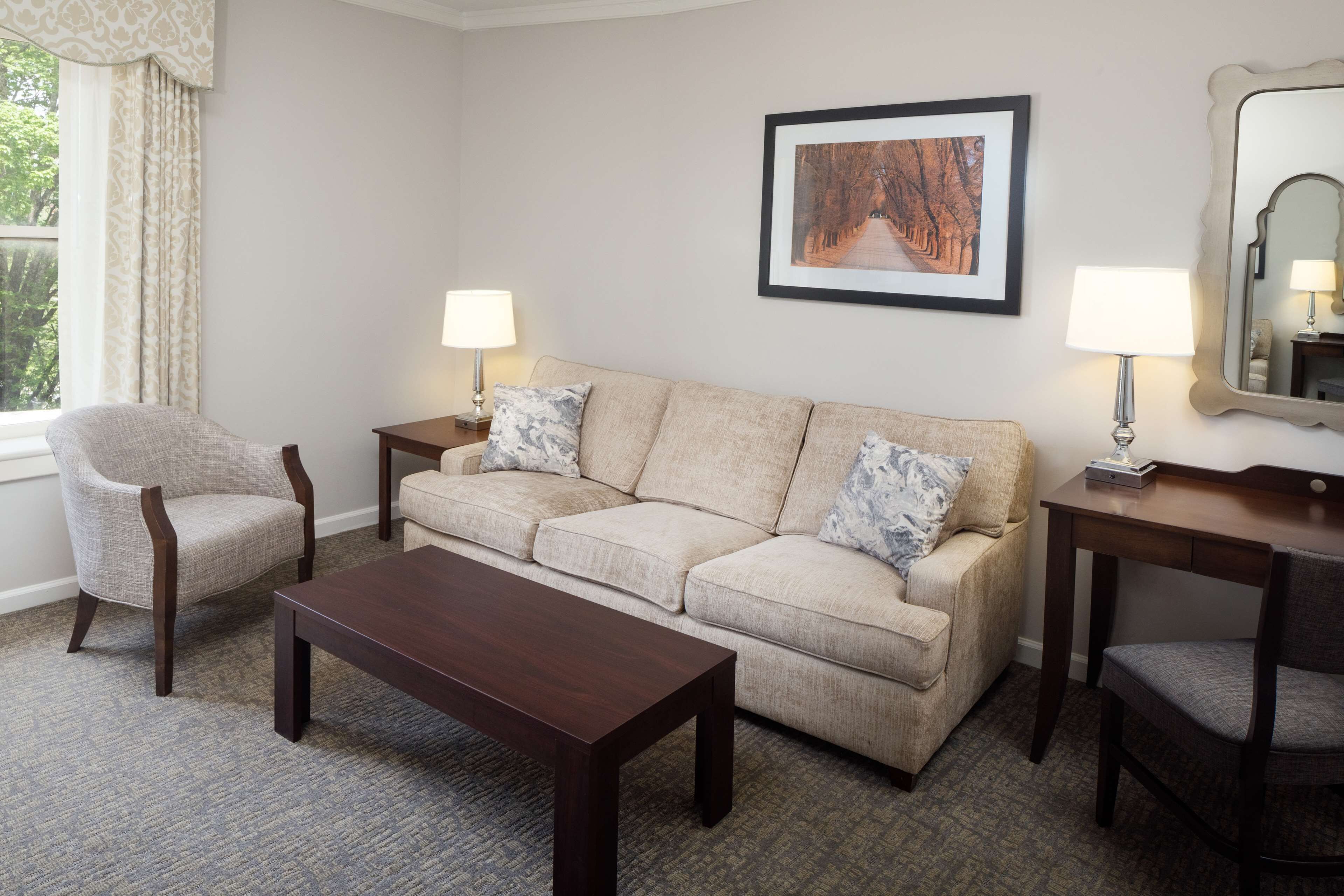 A living room with a sofa, armchairs, a coffee table, lamps, a framed picture, and a mirror.