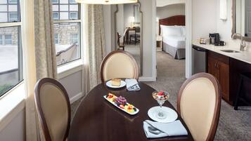 Habitación de hotel con mesa de comedor para dos, cama, baño y vistas al exterior.