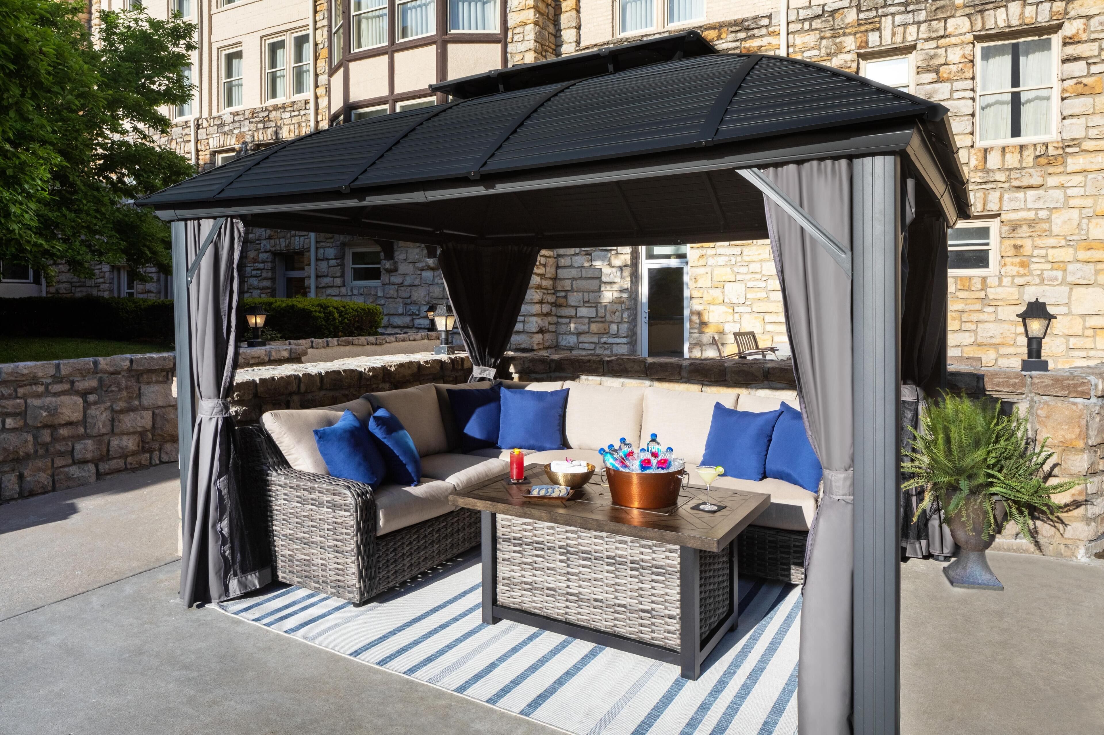 Un espace extérieur aménagé avec un coin salon abrité par un gazebo, des meubles en osier et une table sur laquelle se trouve un seau de glaces.