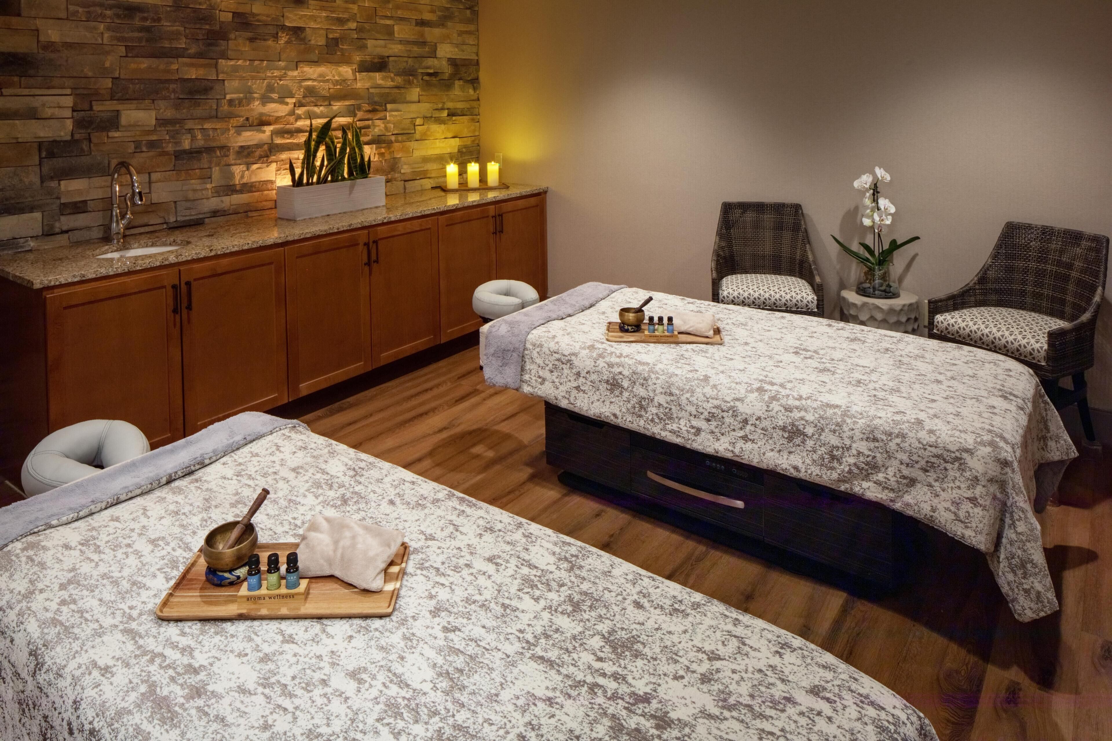 A spa room with two beds, a stone wall, a sink, and a small table with bottles and a bowl.