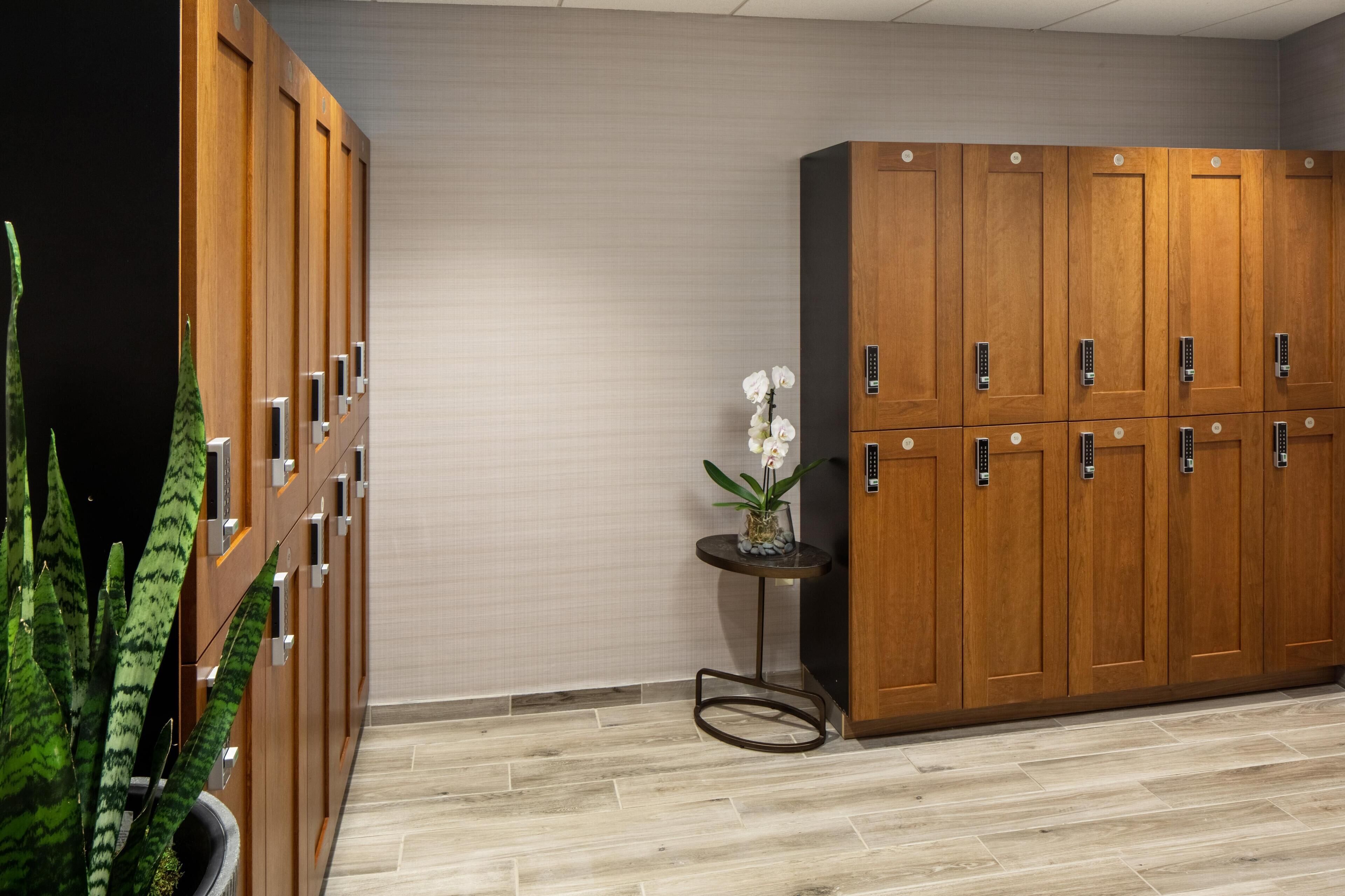 A hotel room with wooden lockers, a small table with a vase of flowers, and a potted plant.