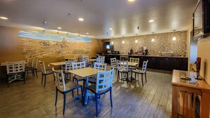 Un restaurante con mesas y sillas de madera, un mural en la pared y una barra con un televisor.