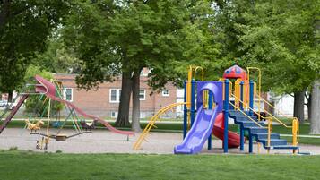 Children can play on the playground's climbing frame, slide, and other structures amidst lush greenery and trees.