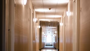 Un largo y estrecho pasillo de hotel con pisos alfombrados y luces en las paredes.