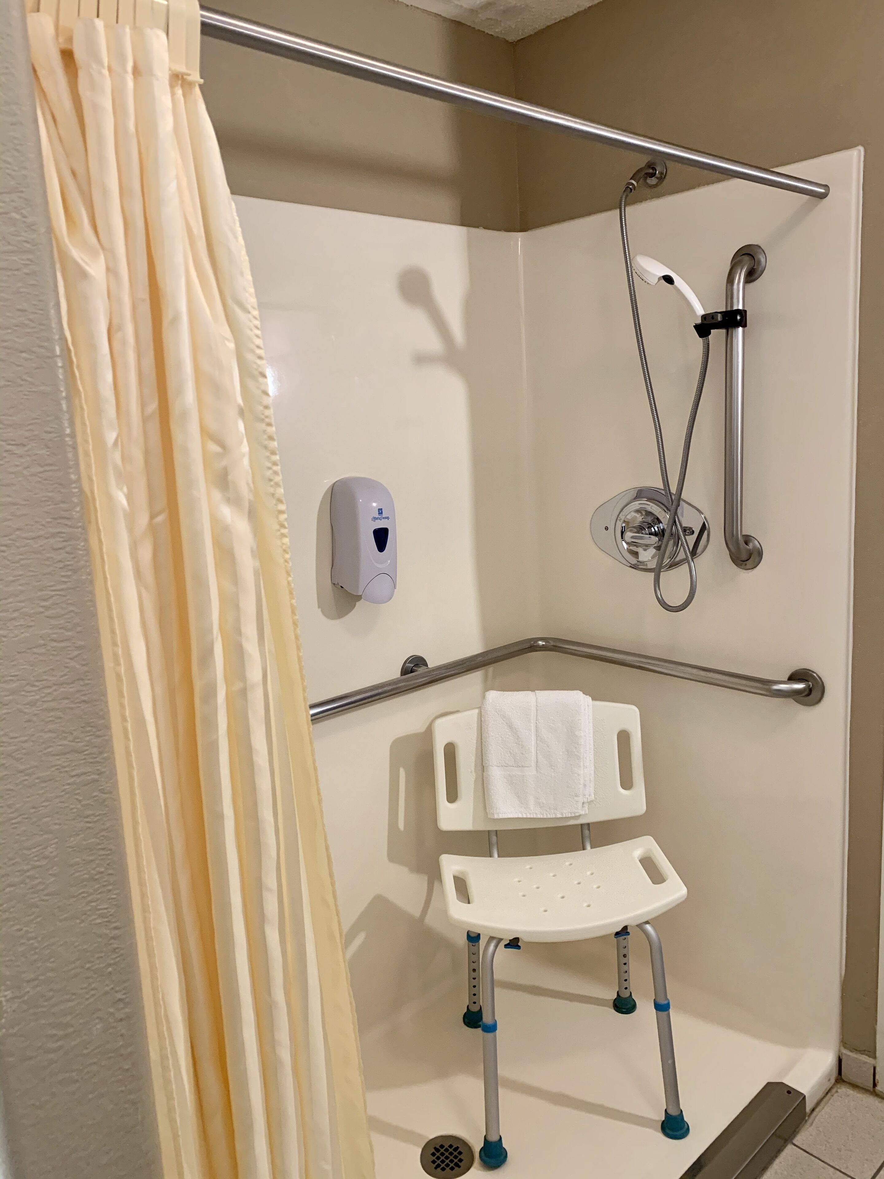 Ein Badezimmer mit Dusche, Haltegriff und einer rollstuhlgerechten Sitzbank.