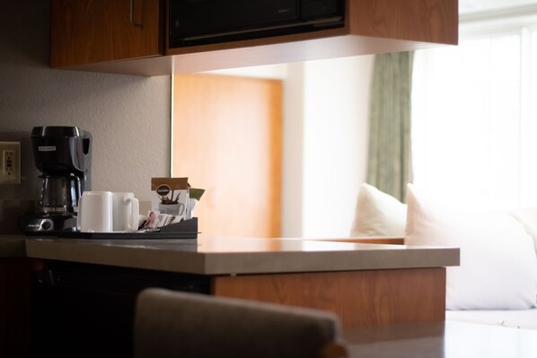A kitchen area with a coffee maker, two white mugs, and a small plant on the counter.